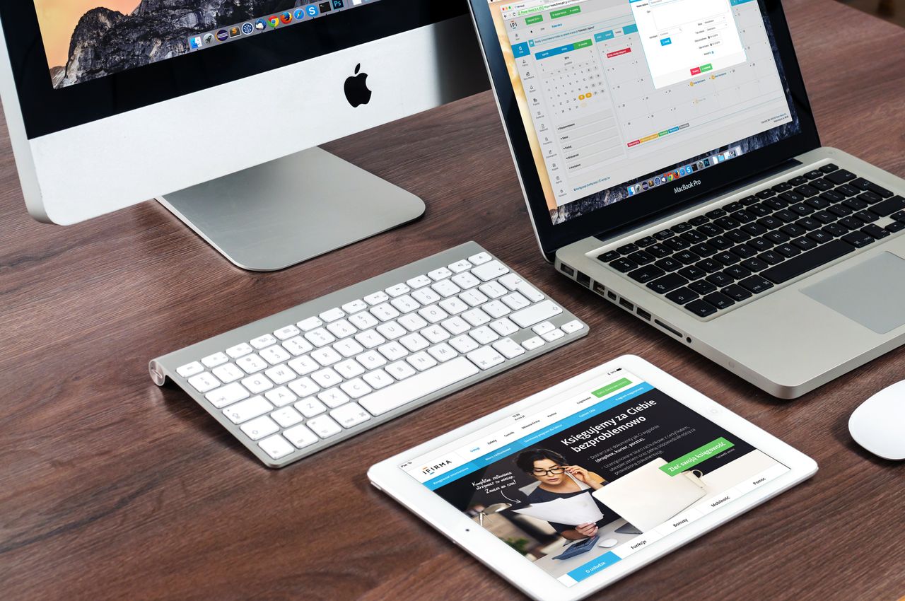 why-choose-us Un bureau de travail élégant présentant des appareils Apple : iMac, MacBook et iPad.